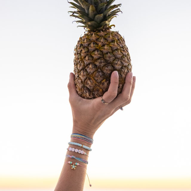 Woman with a colorful bracelet stack of ink blue teal purple holding up a pineapple