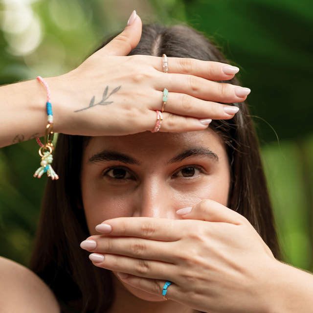 Woman posing with pink cord charm bracelet paired with octopus and stone charms and gold & stone rings