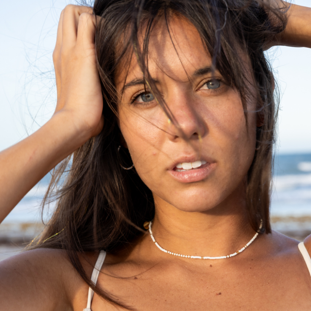 Woman on beach with messy hair wearing a white & gold beaded waterproof choker