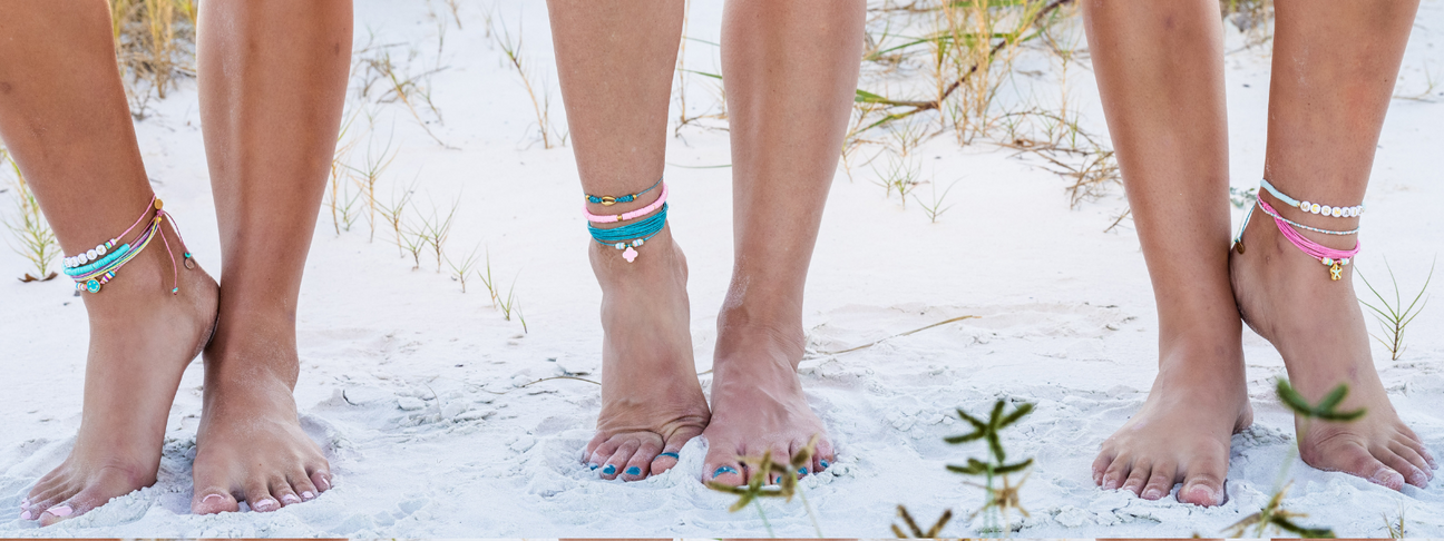 Cute anklets styled three ways, examples of stacking cute colorful anklets, with a sandy beach background