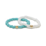 Two beaded rings, one turquoise and one white, with gold beads on a white background.
