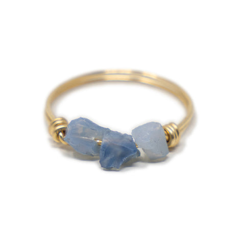 Three blue opal raw cut stones on a gold ring shown on white from the front