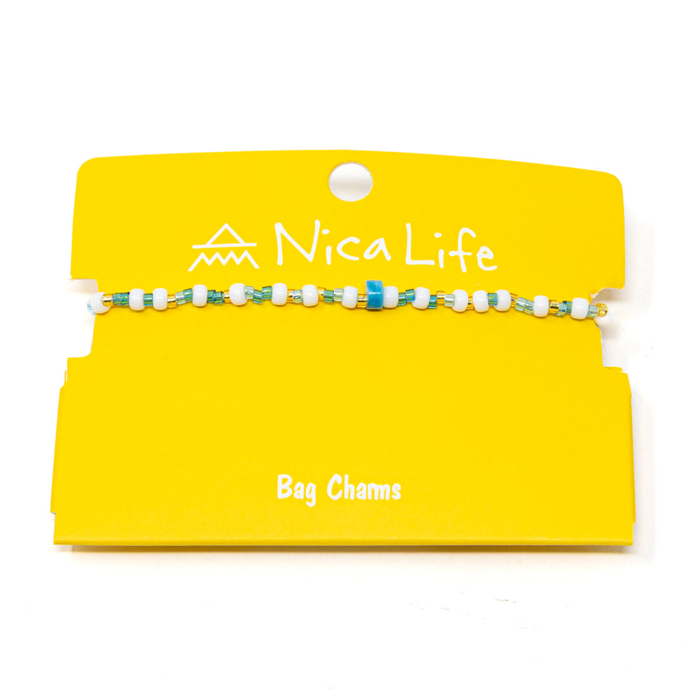 Yellow Nica Life branded card with a blue beaded bag charm on a white background