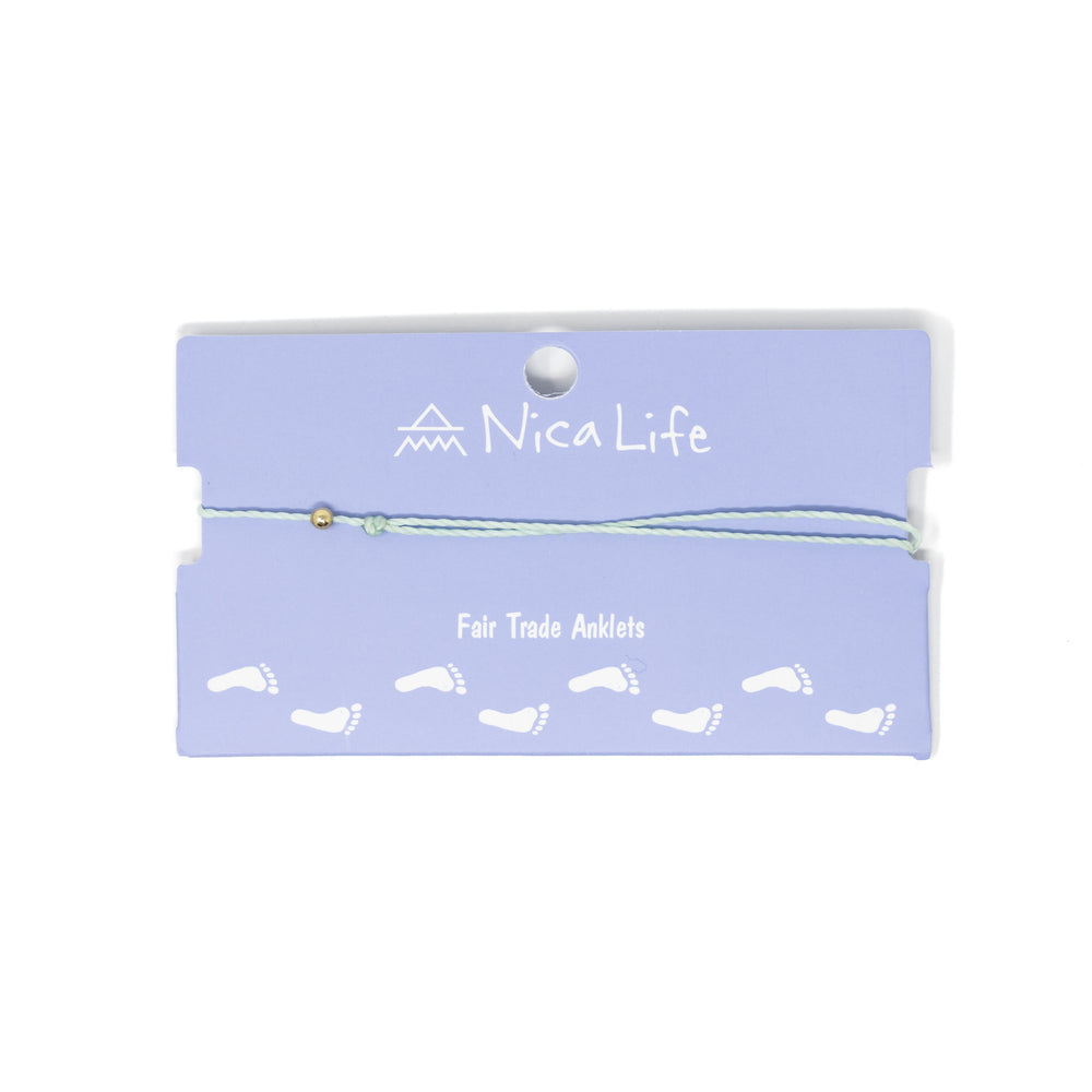 Light mint string anklet with a single gold filled bead on purple Nica Life branded card