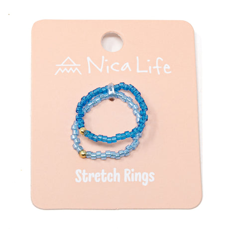 Seed bead stretch rings, dark & light blue luster finsih beads with gold filled bead, on pink card with white. backgrond 