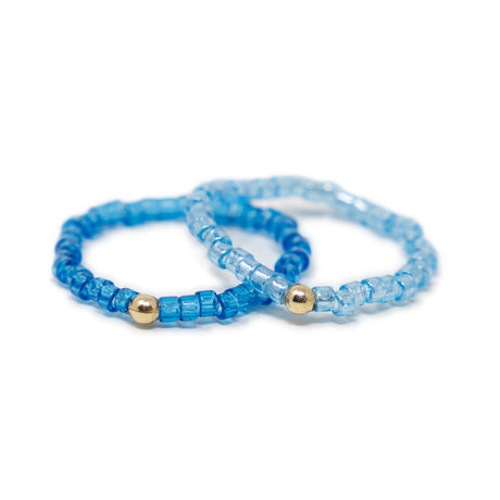 Two cute blue shades of seed bead rings with gold filled bead shown on white