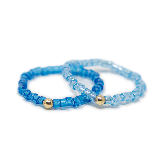 Two cute blue shades of seed bead rings with gold filled bead shown on white