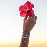 Colorful bracelet stack with bead and string and charms shown on a woman holding a pink/red flower in the air