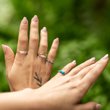 Close-up of hands with multiple rings including stretch, metal and stone, on a blurred leafy green background