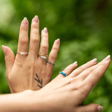 Close-up of hands with multiple rings including stretch, metal and stone, on a blurred leafy green background