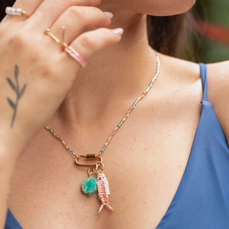 Woman wearing bright beaded charm bar necklace with a two tone pink beaded fish charm and a large amazonite stone charm with hand up wearing pink rings