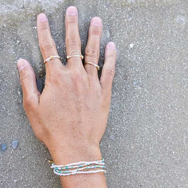 Womans hand  on sand with gold rings and white and colorful stretch bracelets 