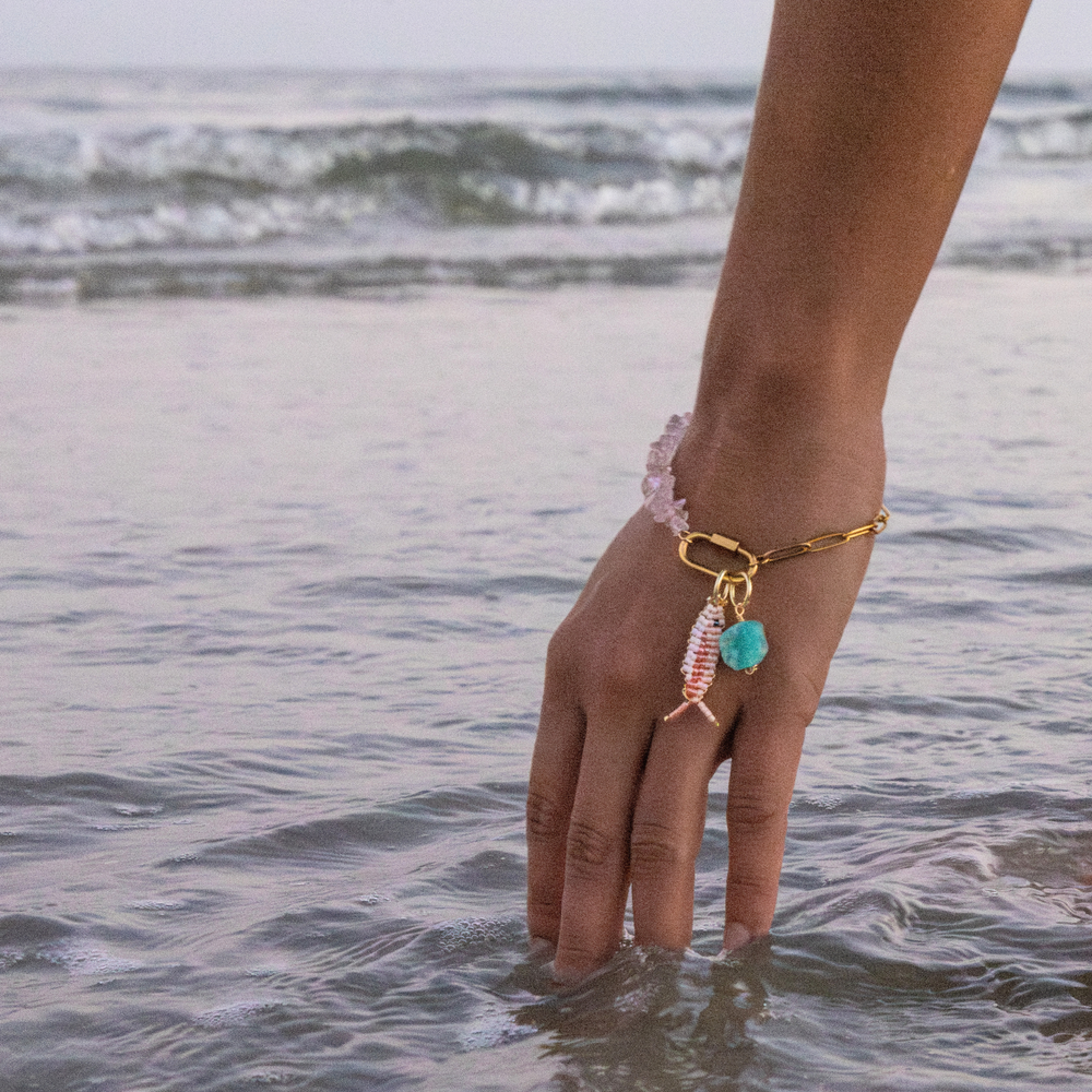 Woman reaching into the water wearing rose quartz & chain charm bracelet with beaded pink fish charm & amazonite stone