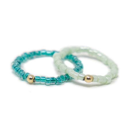 Two shades of green beaded stretch rings with gold beads on a white background