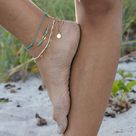 Teal thread ankle bracelet, cucumber shell macrame ankle bracelet & white bead and chain ankle bracelet on model standing on beach