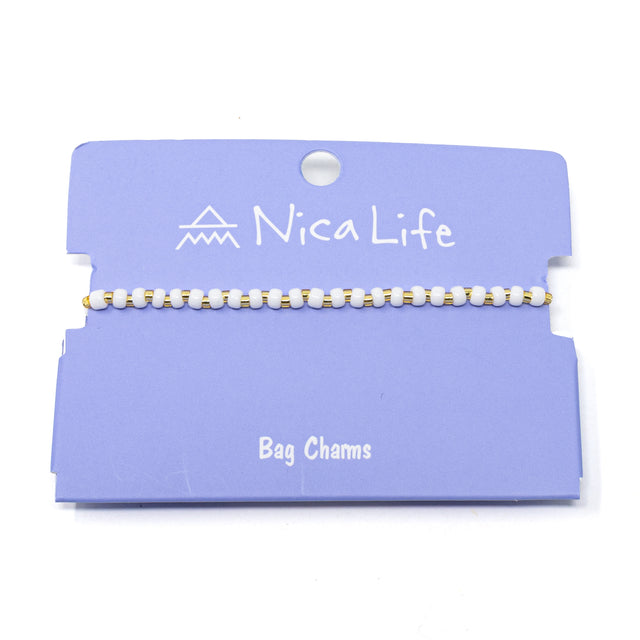 White & gold Nica Life bag charm on a purple card with brand name.