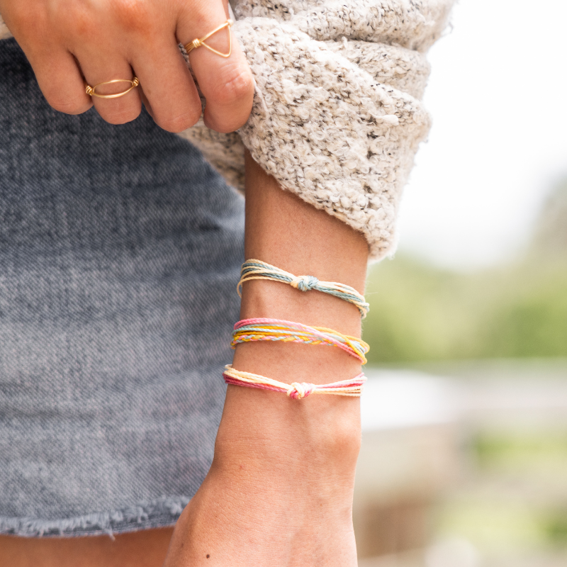Model in a sweater and jean skirt wearing fall bright string bracelets and cold geometric rings standing outside