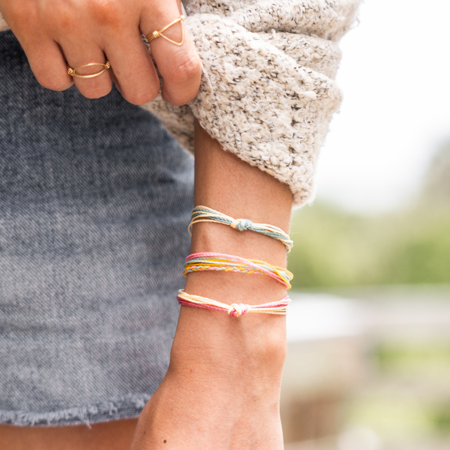 Model in a sweater and jean skirt wearing fall bright string bracelets and cold geometric rings standing outside