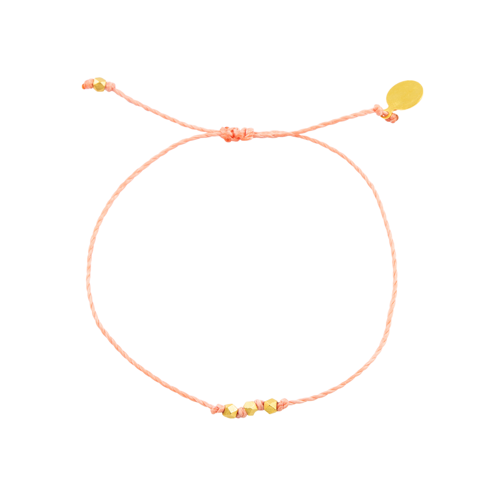 Coral string with gold bead bracelet shown on white top