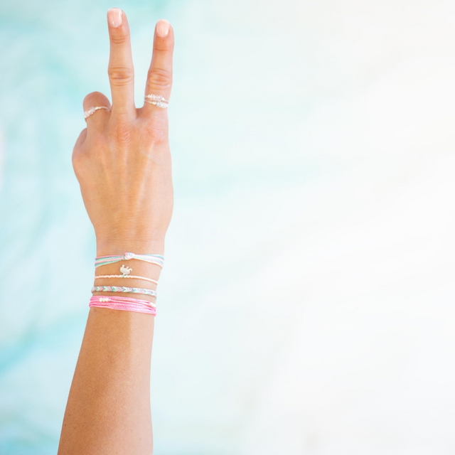 Woman wearing stone rings and pink & teal with silver bracelets in front of a light bluish background